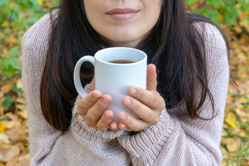 Young woman with pleasure holding mug of hot tea in a hand. Red-haired girl holding her nose, holding a mug of hot tea, on an autumn background.