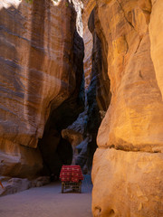 Steep cliffs of a canyon leading to the historical site of Petra, Jordan, light shining from blue sky on dark sandstone walls
