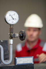 Energy industry. A technician dressed in red overalls and a white helmet checking the heating parameters. Heating water distribution technology. Service work in the power industry.