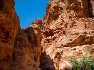 Steep cliffs of a canyon leading to the historical site of Petra, Jordan, light shining from blue sky on dark sandstone walls