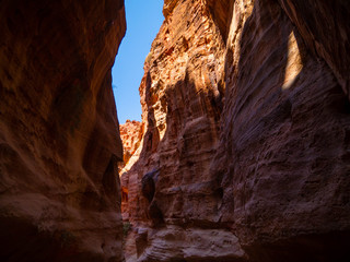 Fototapeta na wymiar Steep cliffs of a canyon leading to the historical site of Petra, Jordan, light shining from blue sky on dark sandstone walls