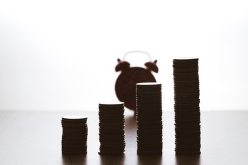 Finance that grows over time. Stack of coins there is a clock on the back. Investment concept. Business and Save Money concept. Dark objects with bright background.