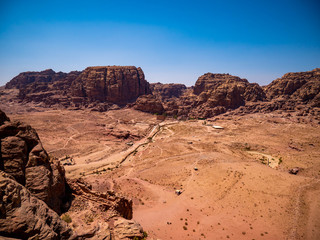 View of the valley of the historic site of Petra, Jordan, orange desert full of temples and a roman amphitheatre, seen from aerial perspective from a sandstone mountain