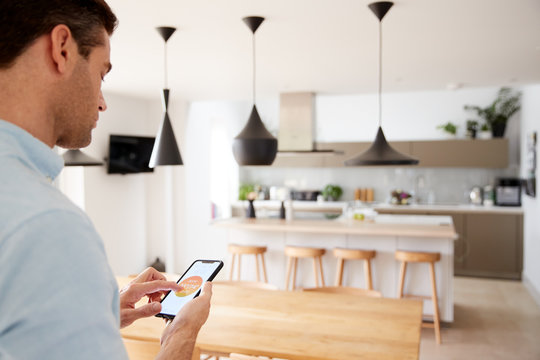 Man Using App On Smart Phone To Control Central Heating Temperature In House