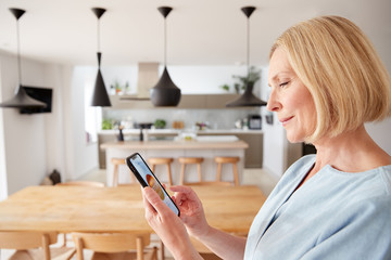Mature Woman Using App On Digital Tablet To Control Central Heating Temperature In House