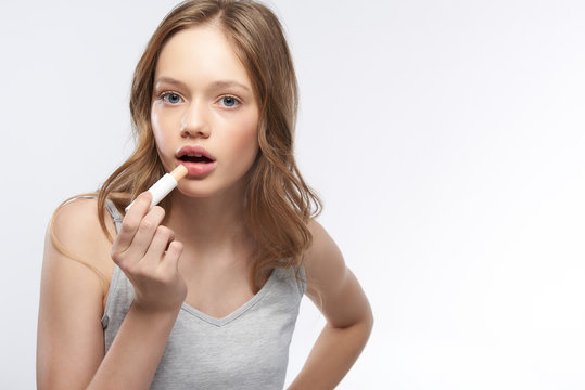 Charming teen girl in tank top using hygienic lipstick