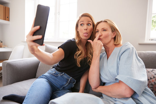 Senior Mother With Adult Daughter Sitting On Sofa Posing For Selfie On Mobile Phone