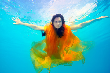 Obraz na płótnie Canvas A beautiful girl underwater with a yellow cloth looks and poses for the camera on a Sunny day, arms outstretched, against the sky. Fashion portrait.