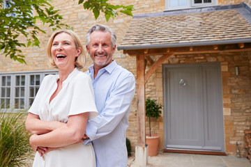 Portrait Of Senior Couple Standing Outside Front Door Of Home