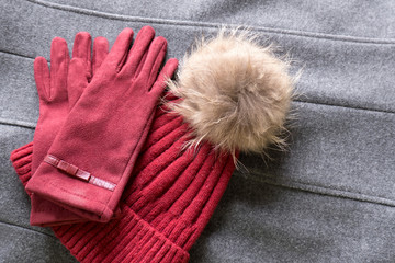 Fototapeta na wymiar Cozy and warm winter flat lay with copy space. Dark red knitted hat with fur pompom and burgundy gloves on gray background
