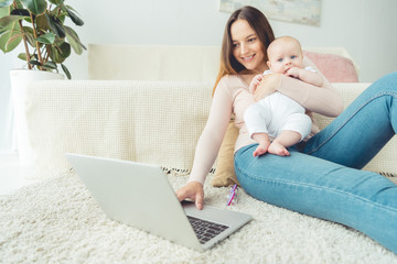 attractive mother holding her child and using laptop in apartment