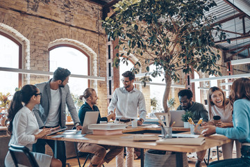 Group of young modern people in smart casual wear communicating and using modern technologies while...