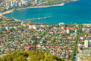 Aerial view of Gelendzhik resort city district from hill of caucasian mountains. Buildings, beaches and blue water of sea bay in frame.