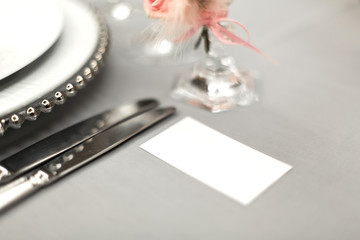 Part of stylish table setting with plate and cutlery. Nearby lies a white business card. Copy space