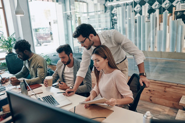 Group of young modern people in smart casual wear communicating and using modern technologies while working in the office