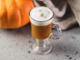Autumn pumpkin latte glass. A warming drink and a knitted scarf on the gray table. Thanksgiving day