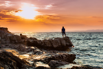Yung man standing on a rock and looking at the sea sunset - Powered by Adobe