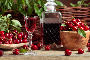 Cherry liquor and red cherries in a wooden bowl on a wooden table in garden.