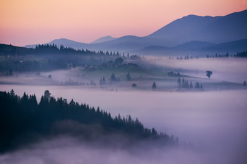 Predawn time in the highlands. A small village among the mountains in the fog, the red sky just before sunset and the silhouettes of the mountains.