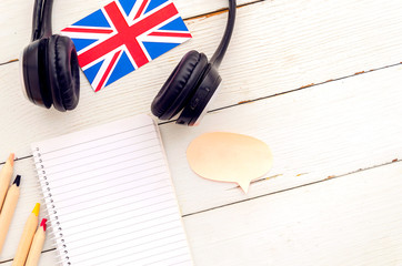 Flat lay frame mockup student learning a language. Desktop made from white wooden planks with blank spiral notebook, earphones and Britsh flag. Top view English language learning concept