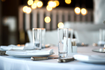 Table setting at a restaurant. Clean glass cup close up. Details of the banquet table. On the background blur are burning garlands with light bulbs