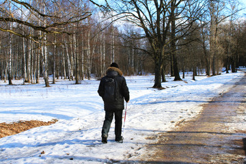 A man in winter clothes with a backpack doing Finnish walking in a winter  park, fuzzy human figure