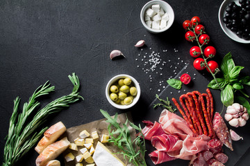 A variety of meat and cheese snacks, sliced jamon and prosciutto, anchovies, olives, feta cheese and brie on a black background. Top view with copy space for your text
