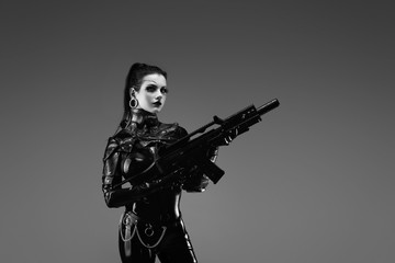 Portrait of a young woman in latex jumpsuit holding a machine gun in her hands	