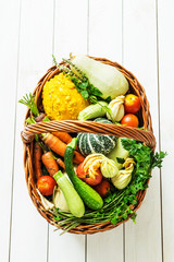 Colorful organic vegetables in wicker basket on white wood