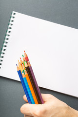 Colored pencils in hand isolated on gray background top view
