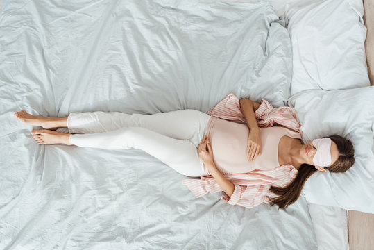top view of smiling pregnant woman lying in bed and touching belly