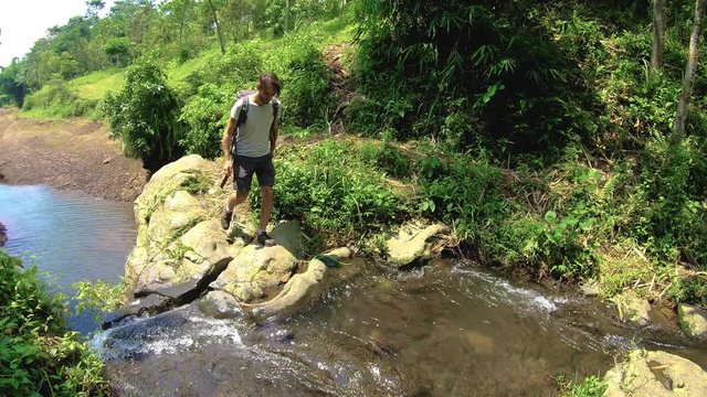 a young man walks up to a mountain river among the jungle on the rocks, and washes fresh cool water on a hot day. 