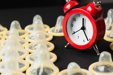red alarm clock with condoms on black background