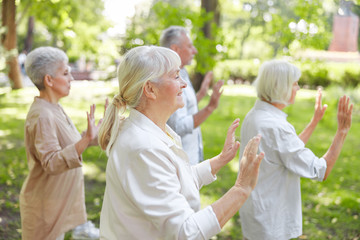 Fototapeta premium Smiling old lady practicing qigong with friends