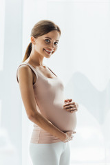 attractive pregnant young woman touching belly and looking at camera