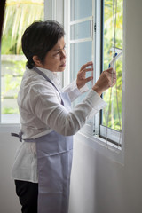 asian middle aged domestic helper woman cleaning windows, doing housework, housekeeping service
