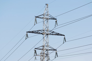 High-voltage technological power lines on metal poles with powerful power wires against the sky