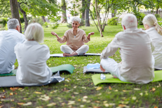 Smiling Senior Lady Teaching Yoga Class In The Park