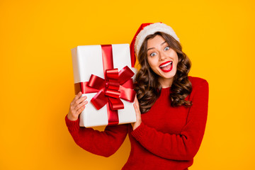 Pretty lady holding big giftbox in hands wear knitted pullover and santa hat isolated yellow background