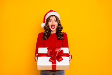 Beautiful lady holding large giftbox in hands wear knitted sweater and santa hat isolated yellow background