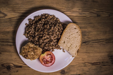 cooked buckwheat, meat cutlet, tomato and bread in a white plate. food background, wooden table