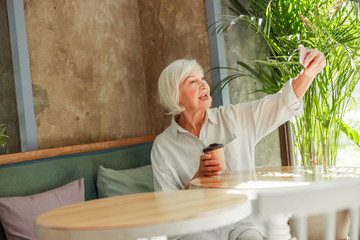 Joyful senior woman making selfie at outdoor cafe
