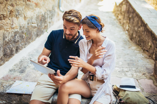 Romantic tourist couple sitting on stairs using digital tablet.
