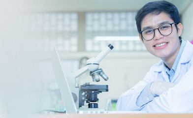 close up asian scientist man wear uniform sitting with microscope on desk to analyze about chemical at laboratory room for research and development about medical and pharmaceutical concept