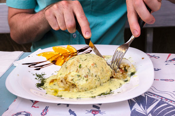 A man with a fork and knife eats stuffed squid in a restaurant
