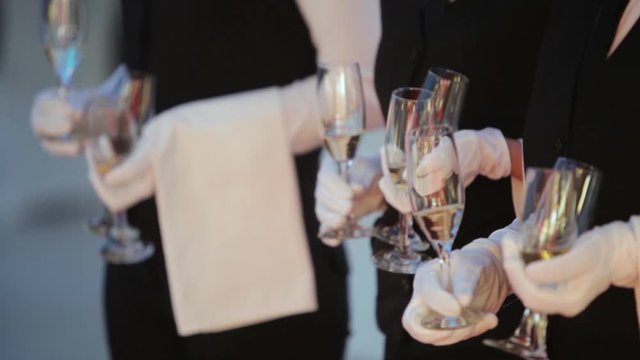 Row of waiters with white gloves and tuxedo serving the high class people. Holding champagne glasses