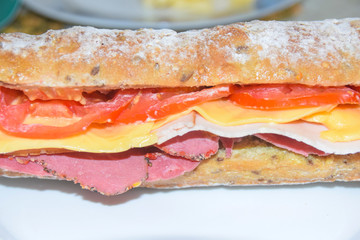Sandwich in a baguette with ham, cheese, chicken and tomato