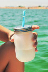 Small bottle with a straw in a female hand on a background of the sea