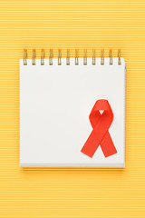 red aids ribbon on open notebook isolated on yellow background