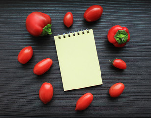  A notebook lies on a table surrounded by red cherry tomatoes and small bell peppers.